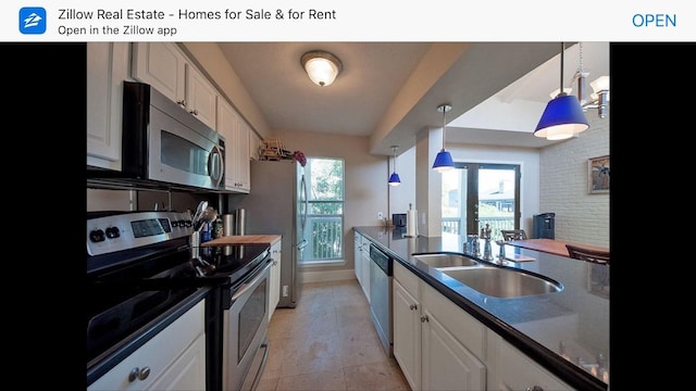 kitchen featuring dark countertops, appliances with stainless steel finishes, decorative light fixtures, white cabinetry, and a sink