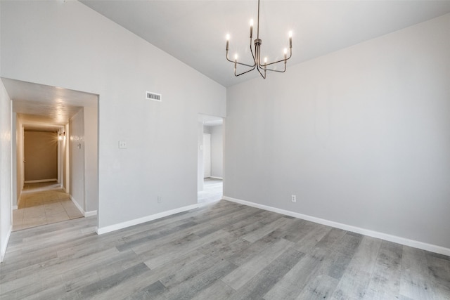 empty room featuring lofted ceiling, a notable chandelier, visible vents, baseboards, and light wood-type flooring