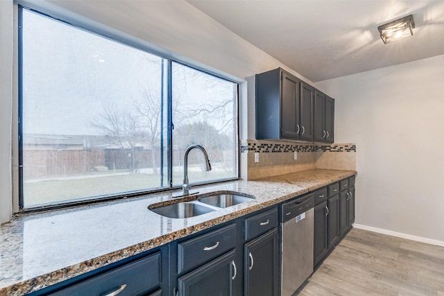 kitchen featuring decorative backsplash, dishwasher, light stone countertops, light wood-style floors, and a sink