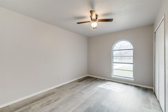 empty room with a ceiling fan, light wood-type flooring, and baseboards