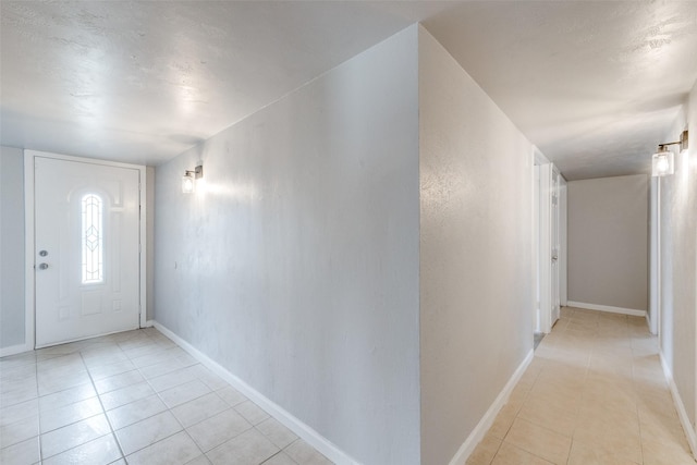 foyer with light tile patterned floors, a textured wall, and baseboards