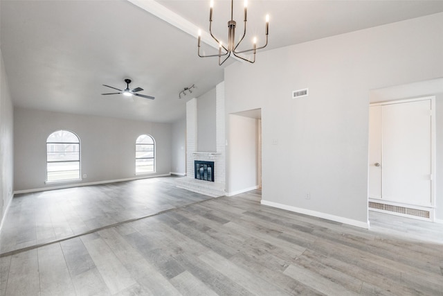 unfurnished living room featuring light wood finished floors, baseboards, visible vents, a fireplace, and high vaulted ceiling