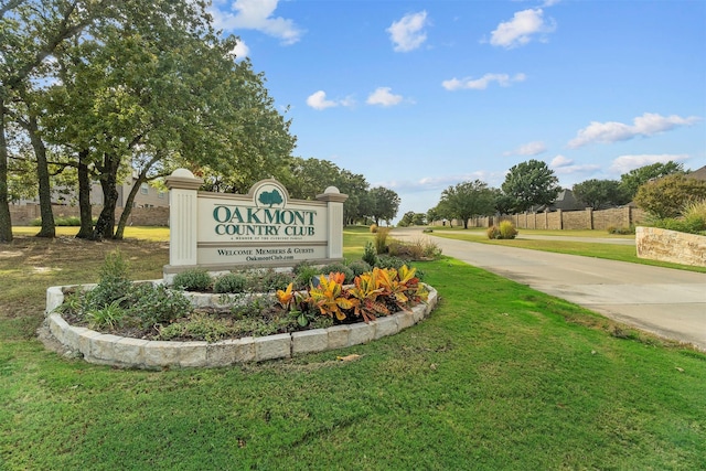 community sign featuring a lawn and concrete driveway