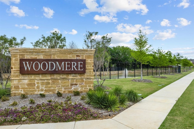 community / neighborhood sign featuring fence and a lawn