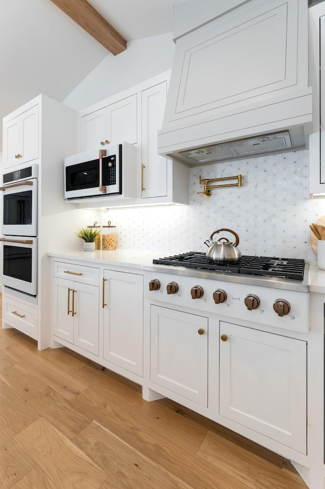 kitchen featuring white appliances, tasteful backsplash, white cabinets, custom range hood, and light countertops