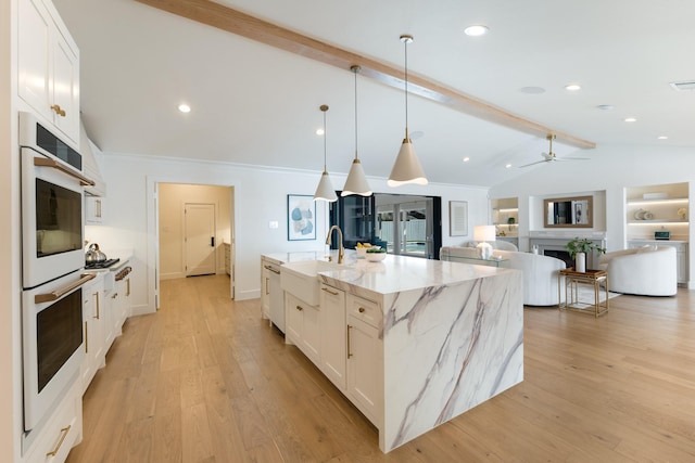 kitchen with vaulted ceiling with beams, double oven, a fireplace, a sink, and light wood-type flooring