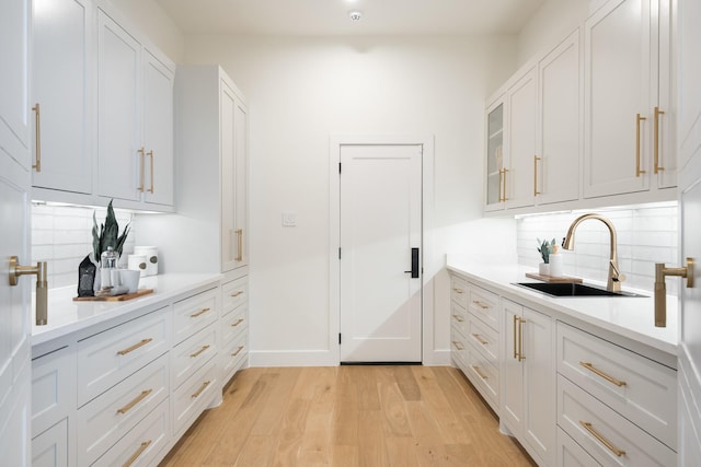 interior space featuring tasteful backsplash, a sink, light wood-style flooring, and baseboards