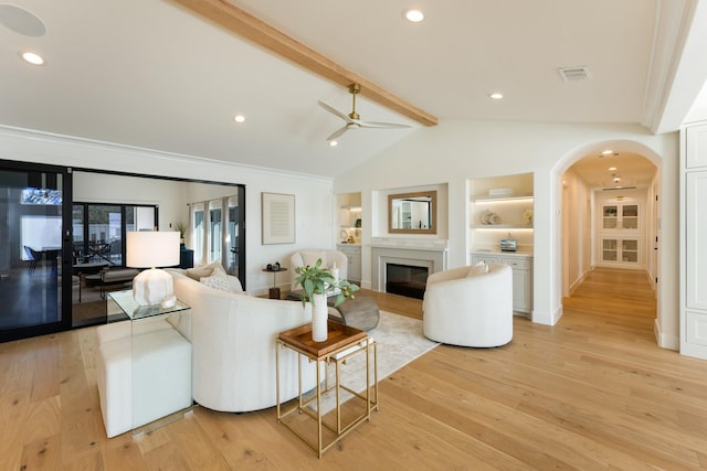 living room featuring lofted ceiling with beams, light wood-style flooring, arched walkways, and a glass covered fireplace