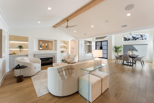 living room featuring arched walkways, light wood-type flooring, a glass covered fireplace, and visible vents