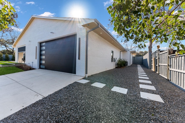 view of property exterior featuring a garage, driveway, fence, and brick siding