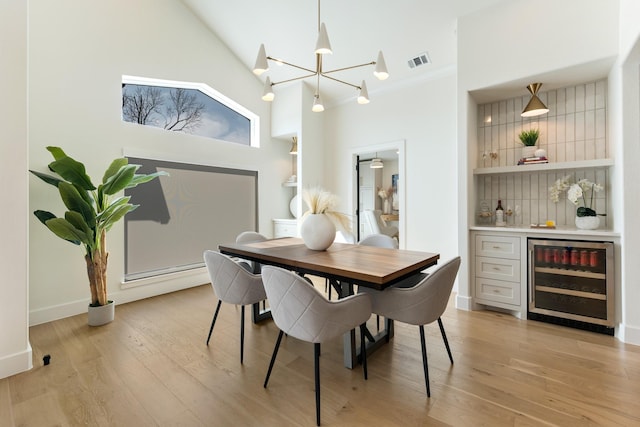 dining area featuring a chandelier, wine cooler, light wood-style flooring, visible vents, and a bar