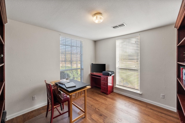 home office with visible vents, baseboards, a textured ceiling, and wood finished floors