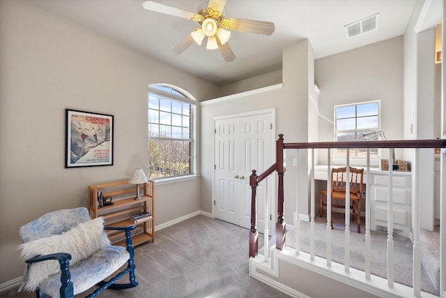 living area with a ceiling fan, baseboards, visible vents, carpet floors, and an upstairs landing