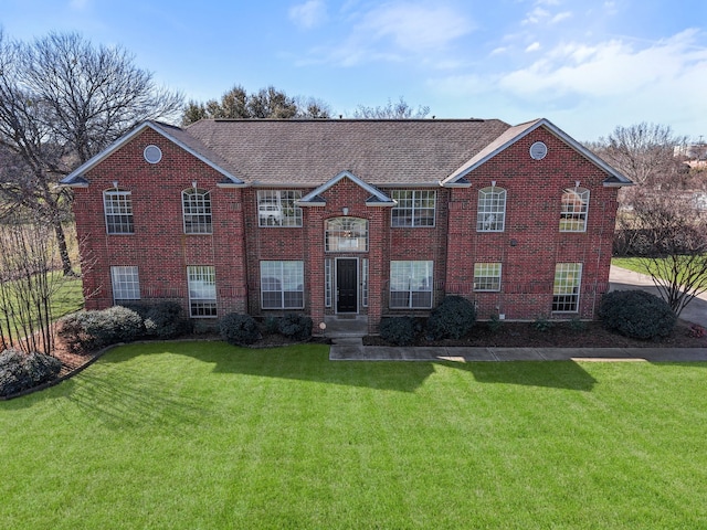 view of front of house with a front yard, brick siding, and a shingled roof