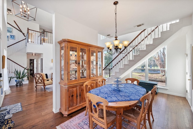 dining area with visible vents, a notable chandelier, wood finished floors, and stairs