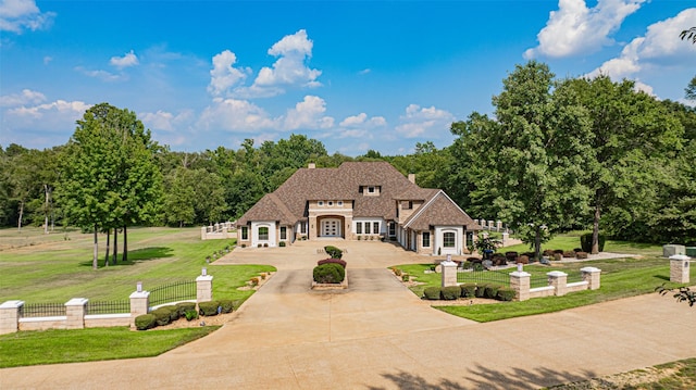 french country home featuring a fenced front yard, concrete driveway, stone siding, and a front lawn