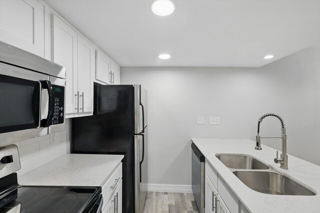 kitchen with white cabinets, light wood-style flooring, appliances with stainless steel finishes, light stone countertops, and a sink