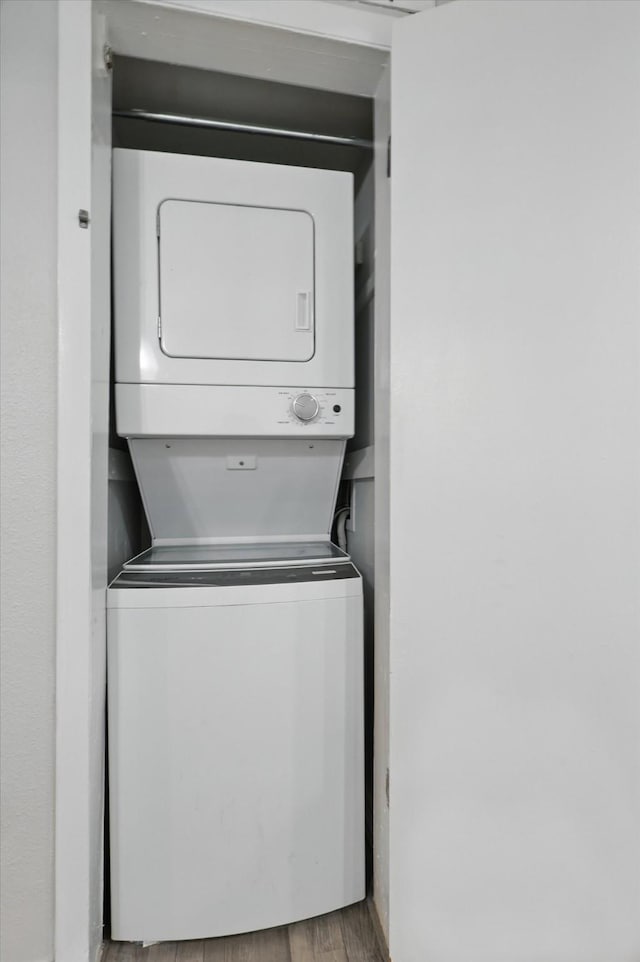 clothes washing area with stacked washer / drying machine, laundry area, and wood finished floors