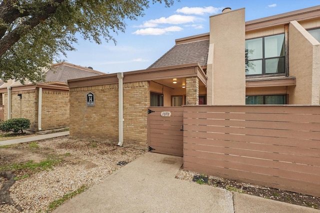 view of side of home with a shingled roof, a chimney, fence, and stucco siding