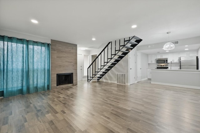 unfurnished living room with light wood-style flooring, stairway, a fireplace, and visible vents