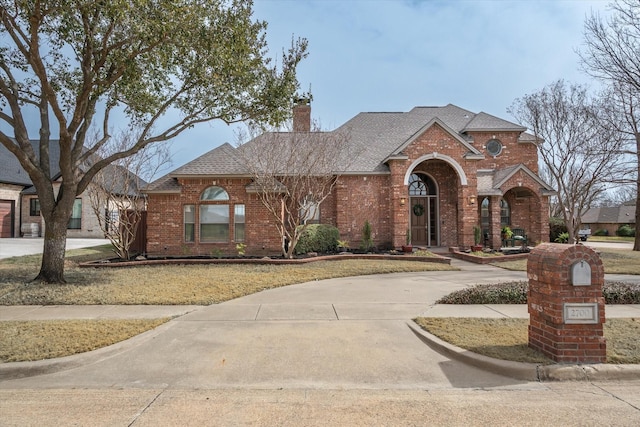 view of front of property with driveway, brick siding, a chimney, and a shingled roof