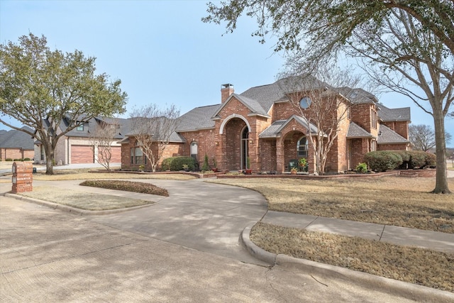 view of front facade featuring concrete driveway, brick siding, a chimney, and roof with shingles