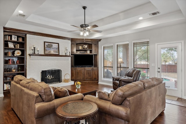 living area featuring a brick fireplace, visible vents, a raised ceiling, and dark wood finished floors