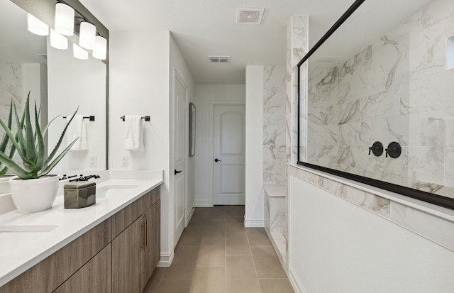 full bath with tile patterned flooring, a sink, visible vents, a marble finish shower, and double vanity