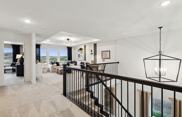 corridor featuring visible vents, a tray ceiling, an upstairs landing, carpet floors, and a notable chandelier