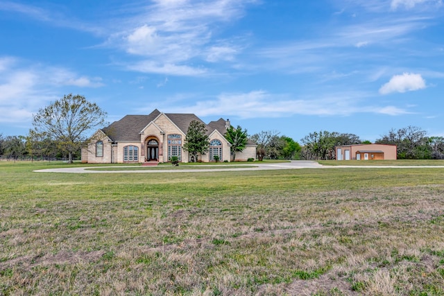french country home with a front lawn, a detached garage, brick siding, and concrete driveway