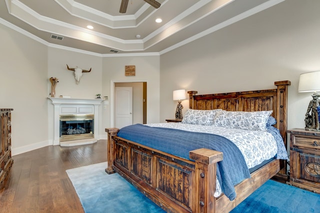 bedroom with crown molding, a tray ceiling, visible vents, a glass covered fireplace, and wood finished floors