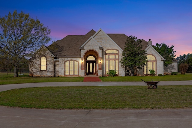 french country home featuring stone siding, a chimney, brick siding, curved driveway, and a yard
