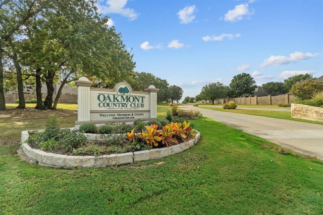 community sign with concrete driveway and a lawn