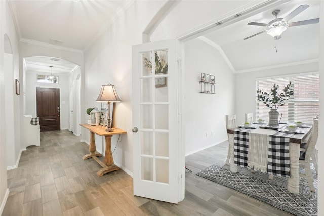 corridor featuring baseboards, arched walkways, ornamental molding, wood finished floors, and vaulted ceiling