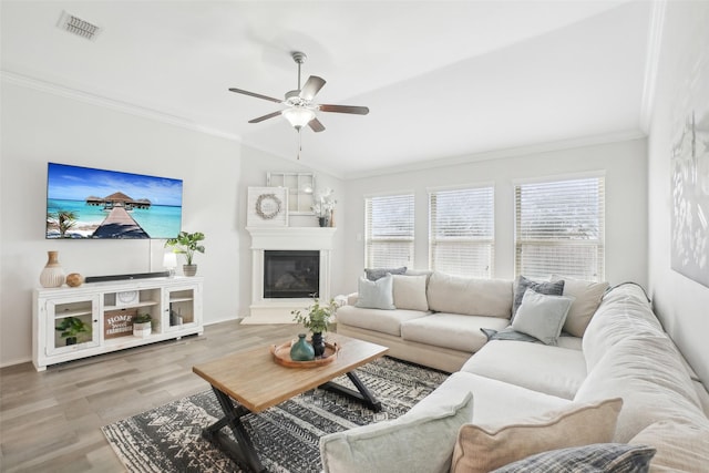 living room featuring visible vents, wood finished floors, a glass covered fireplace, crown molding, and ceiling fan