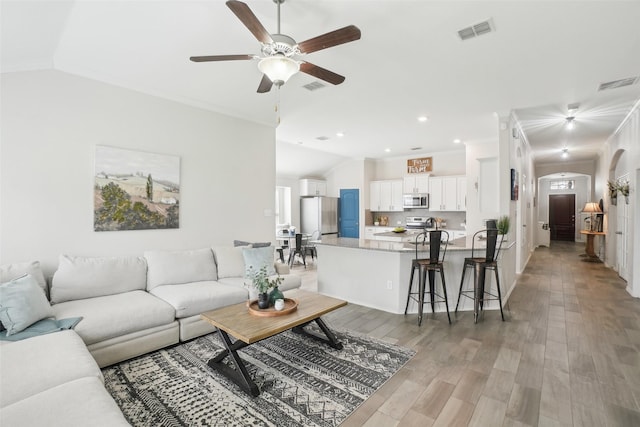 living room featuring arched walkways, light wood finished floors, and visible vents