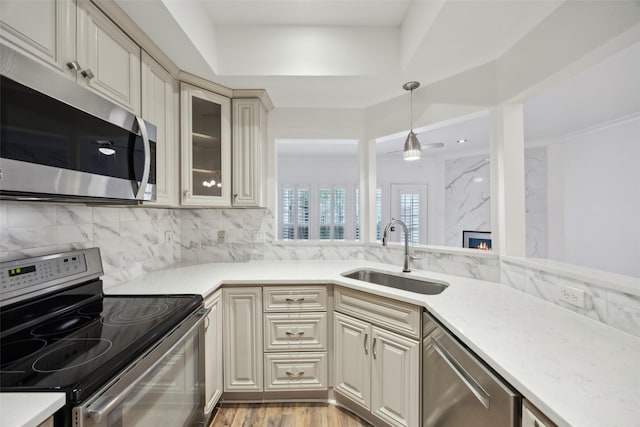 kitchen featuring decorative backsplash, glass insert cabinets, appliances with stainless steel finishes, cream cabinetry, and a sink