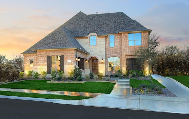 view of front of house featuring a shingled roof, a front yard, stone siding, and brick siding