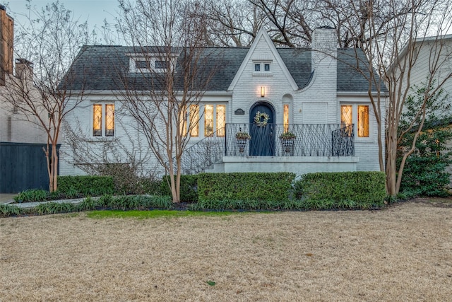 english style home with a shingled roof, a front yard, a chimney, and brick siding