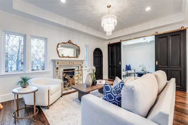 living area with a tray ceiling, a fireplace, an inviting chandelier, a barn door, and wood finished floors