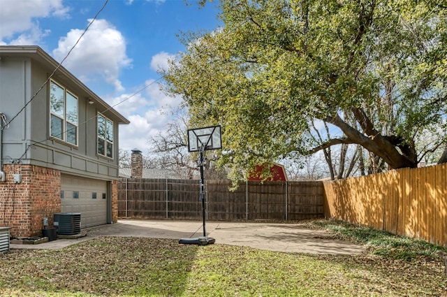 view of yard with concrete driveway, central AC, fence, and an attached garage