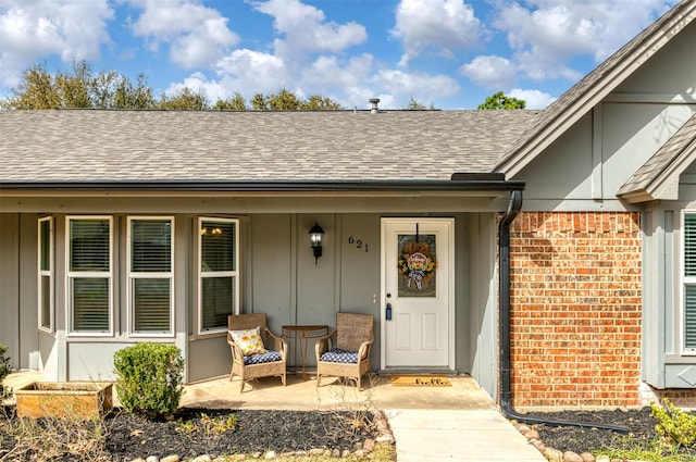 property entrance featuring a porch, brick siding, board and batten siding, and roof with shingles