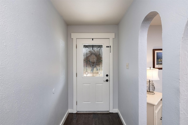 doorway to outside featuring arched walkways, dark wood finished floors, and baseboards