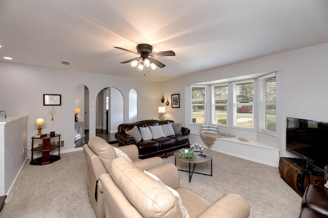 carpeted living room with baseboards, visible vents, arched walkways, and a ceiling fan