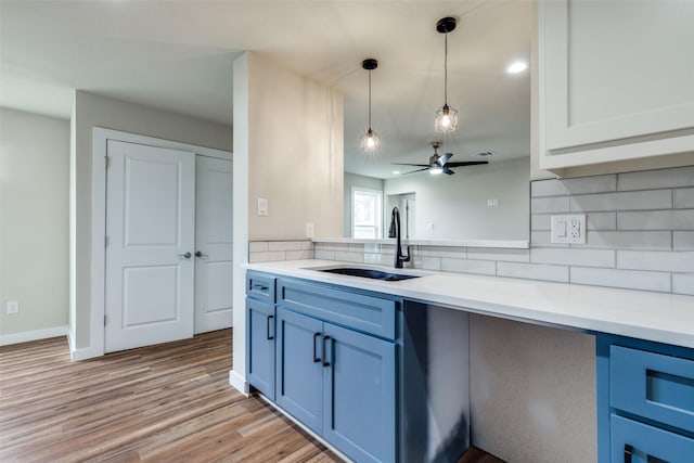 kitchen with pendant lighting, tasteful backsplash, light countertops, a sink, and light wood-type flooring