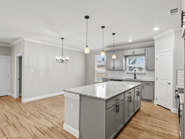 kitchen featuring wood finish floors, tasteful backsplash, gray cabinets, a sink, and a kitchen island