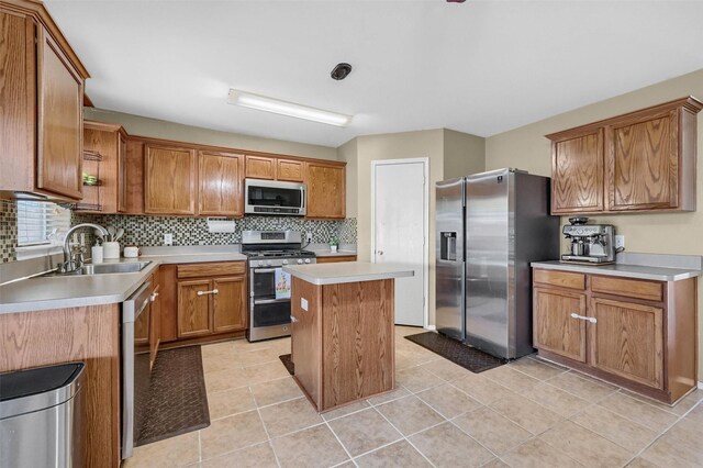 kitchen with brown cabinetry, decorative backsplash, appliances with stainless steel finishes, a center island, and a sink