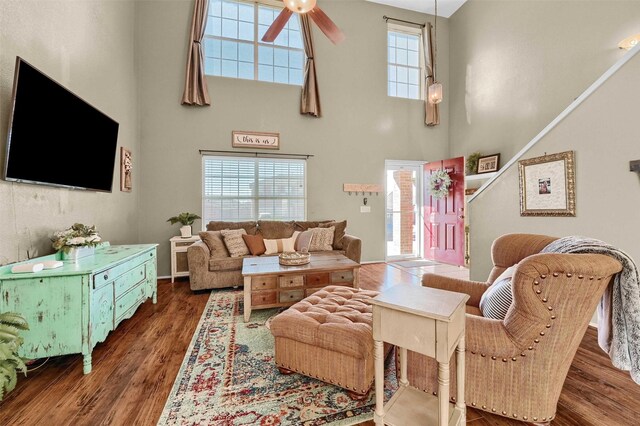 living area with ceiling fan, a high ceiling, stairway, and wood finished floors