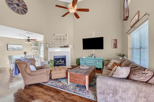 living area featuring a fireplace, visible vents, a towering ceiling, ceiling fan, and wood finished floors