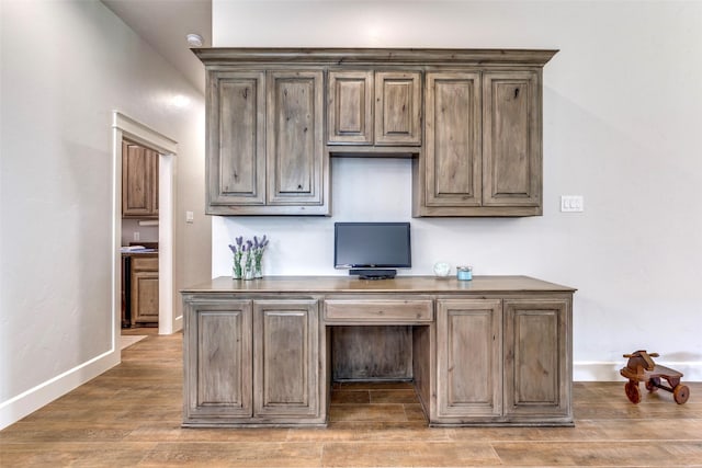 interior space featuring built in desk, baseboards, and wood finished floors